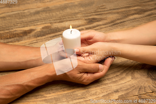 Image of Hands guarding, holding a white candle on wooden background with copyspace