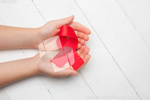 Image of Female and male hands holding red HIV and AIDS awareness ribbon isolated on wooden background