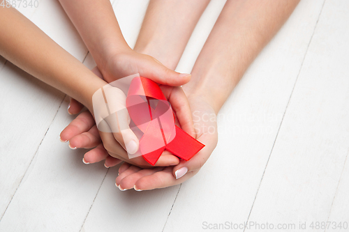 Image of Female and male hands holding red HIV and AIDS awareness ribbon isolated on wooden background