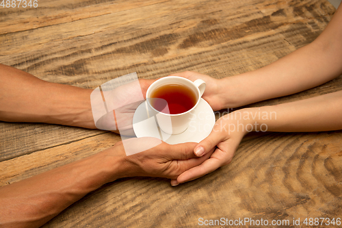 Image of Hands of couple holding mug of tea, top view on wooden background with copyspace