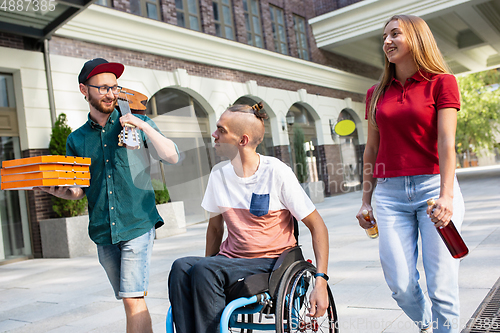 Image of Group of friends taking a stroll on city\'s street in summer day