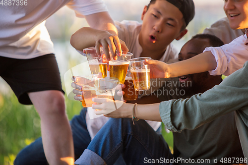 Image of Group of friends clinking beer glasses during picnic at the beach. Lifestyle, friendship, having fun, weekend and resting concept.