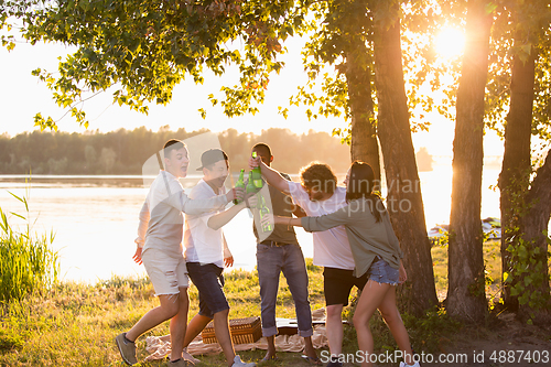 Image of Group of friends clinking beer bottles during picnic at the beach. Lifestyle, friendship, having fun, weekend and resting concept.