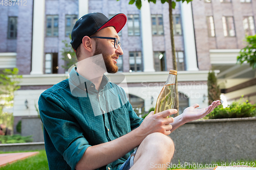 Image of Beautiful stylish young man holding drink and relaxing in city street