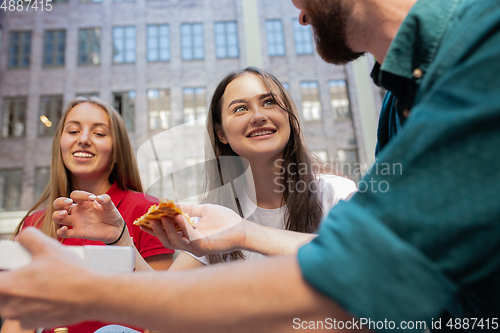 Image of Tourists, friends enjoying pizza on street and smiling. Summertime, fast food