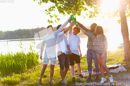 Image of Group of friends clinking beer bottles during picnic at the beach. Lifestyle, friendship, having fun, weekend and resting concept.