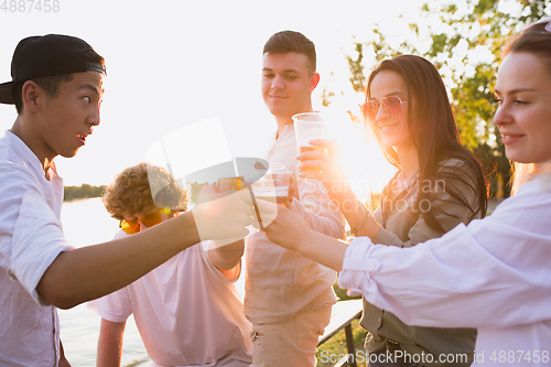 Image of Group of friends clinking beer glasses during picnic at the beach. Lifestyle, friendship, having fun, weekend and resting concept.