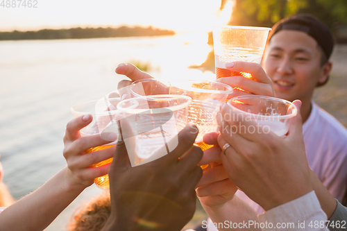 Image of Group of friends clinking beer glasses during picnic at the beach. Lifestyle, friendship, having fun, weekend and resting concept.