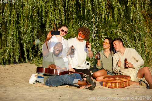 Image of Group of friends clinking beer glasses during picnic at the beach. Lifestyle, friendship, having fun, weekend and resting concept.