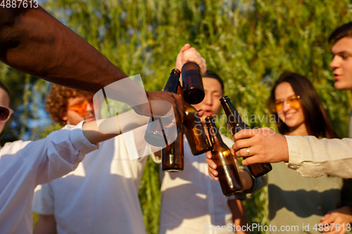 Image of Group of friends clinking beer glasses during picnic at the beach. Lifestyle, friendship, having fun, weekend and resting concept.