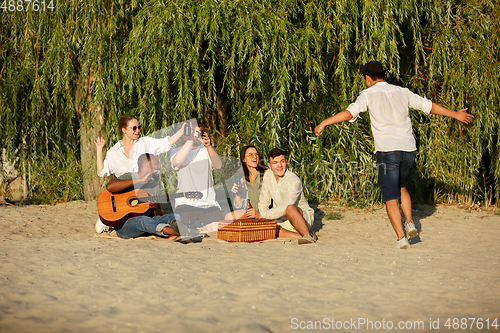 Image of Group of friends clinking beer glasses during picnic at the beach. Lifestyle, friendship, having fun, weekend and resting concept.