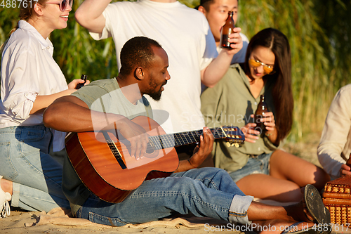 Image of Group of friends clinking beer glasses during picnic at the beach. Lifestyle, friendship, having fun, weekend and resting concept.