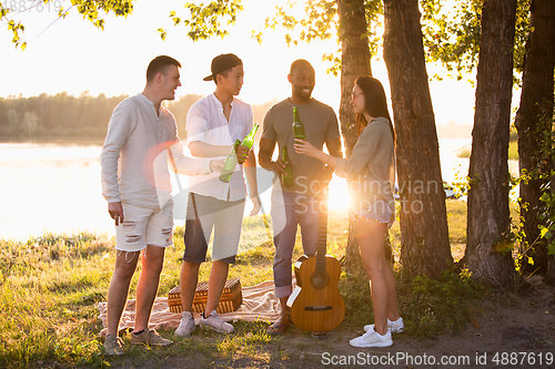 Image of Group of friends clinking beer glasses during picnic at the beach. Lifestyle, friendship, having fun, weekend and resting concept.