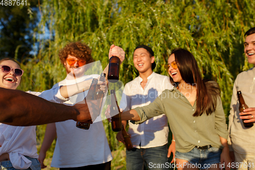 Image of Group of friends clinking beer glasses during picnic at the beach. Lifestyle, friendship, having fun, weekend and resting concept.