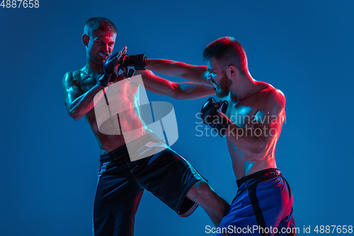 Image of MMA. Two professional fighters punching or boxing isolated on blue studio background in neon