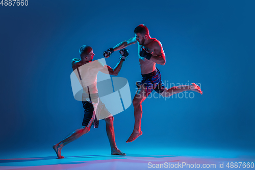 Image of MMA. Two professional fighters punching or boxing isolated on blue studio background in neon