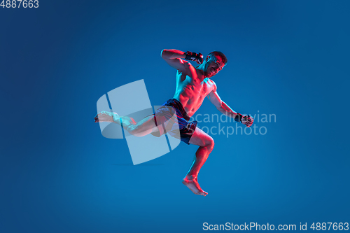 Image of MMA. Professional fighter punching or boxing isolated on blue studio background in neon