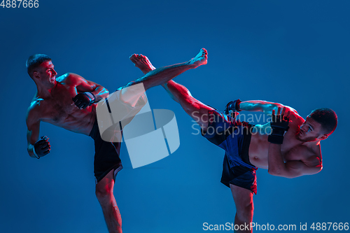 Image of MMA. Two professional fighters punching or boxing isolated on blue studio background in neon