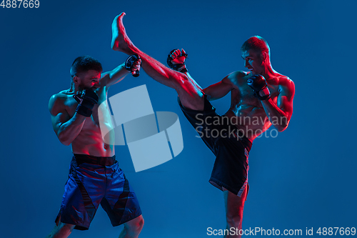 Image of MMA. Two professional fighters punching or boxing isolated on blue studio background in neon