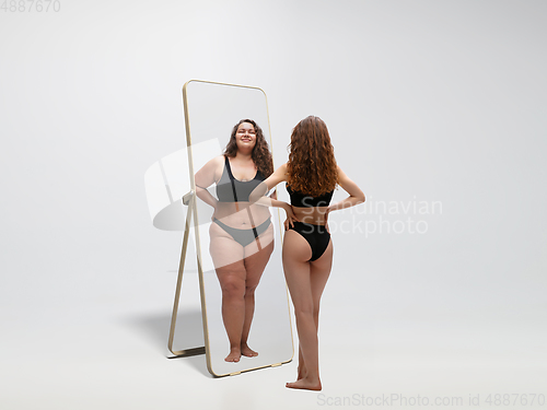 Image of Young fit, slim woman looking at fat girl in mirror\'s reflection on white background