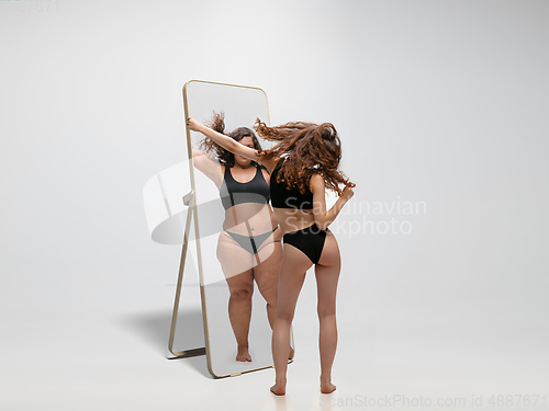 Image of Young fit, slim woman looking at fat girl in mirror\'s reflection on white background