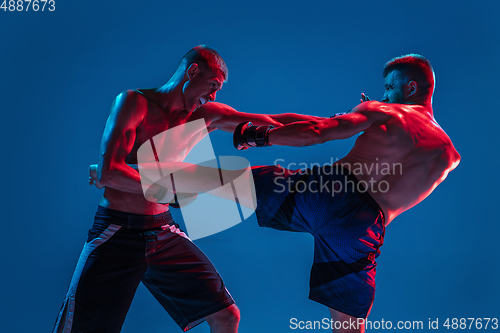 Image of MMA. Two professional fighters punching or boxing isolated on blue studio background in neon