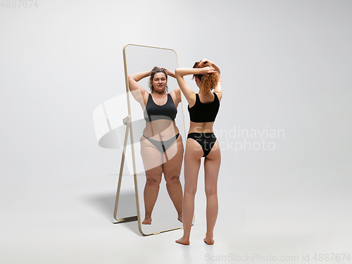 Image of Young fit, slim woman looking at fat girl in mirror\'s reflection on white background