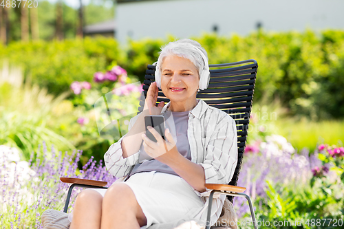 Image of old woman with headphones and smartphone at garden