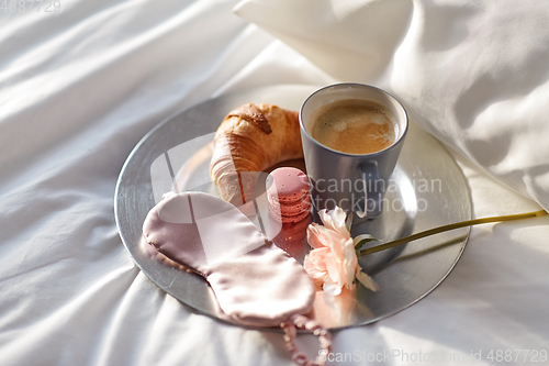 Image of croissant, coffee and eye sleeping mask in bed