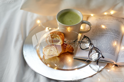 Image of croissants, matcha tea, book and glasses in bed