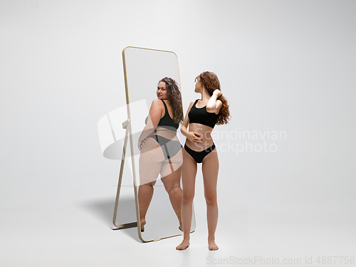 Image of Young fit, slim woman looking at fat girl in mirror\'s reflection on white background