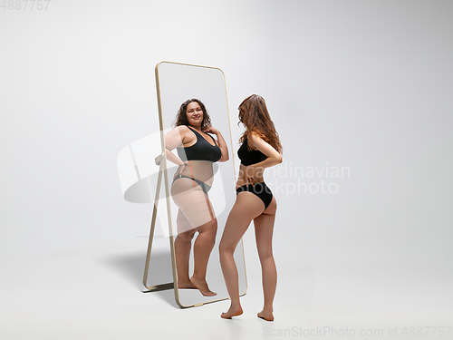 Image of Young fit, slim woman looking at fat girl in mirror\'s reflection on white background