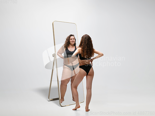 Image of Young fit, slim woman looking at fat girl in mirror\'s reflection on white background