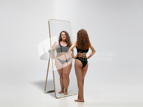 Image of Young fit, slim woman looking at fat girl in mirror\'s reflection on white background