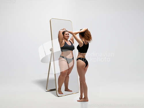 Image of Young fit, slim woman looking at fat girl in mirror\'s reflection on white background