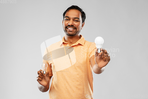 Image of smiling indian man comparing different light bulbs
