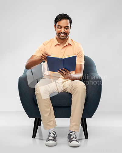 Image of happy young indian man reading book in chair