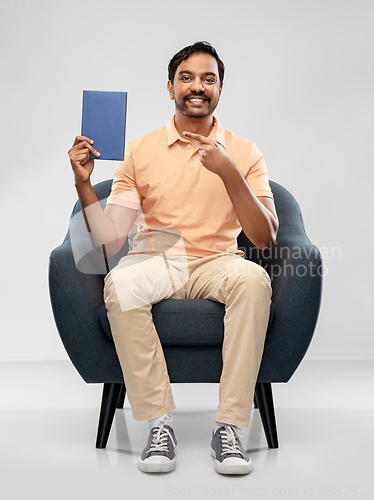 Image of happy young indian man showing book in chair