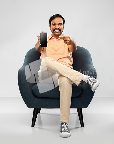 Image of happy young indian man showing smartphone in chair