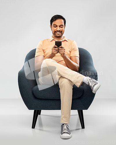 Image of happy young indian man with smartphone in chair