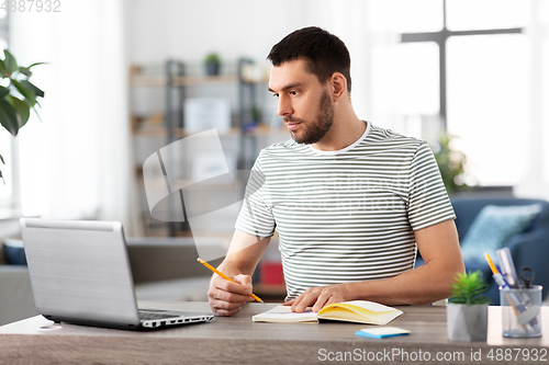 Image of man with notebook and laptop at home office