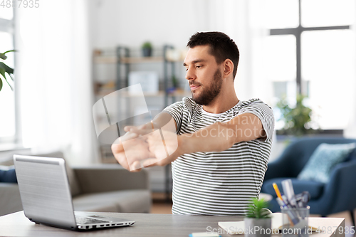 Image of man with laptop stretching at home office