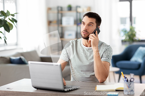 Image of man with laptop calling on phone at home office