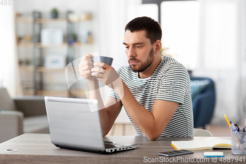 Image of man with laptop drinking coffee at home office