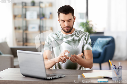 Image of man using hand sanitizer at home office