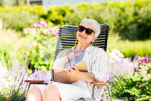 Image of happy senior woman with diary at summer garden