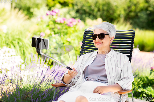 Image of happy senior woman taking selfie at summer garden