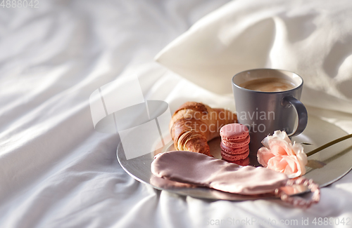 Image of croissant, coffee and eye sleeping mask in bed