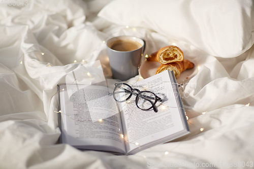 Image of croissants, cup of coffee, book and glasses in bed