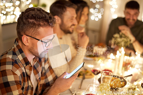 Image of man with smartphone at dinner party with friends
